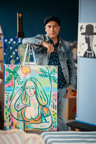 Pedro standing behind a painting of a women on the beach